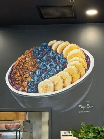 Wall mural of a large acai bowl topped with granola, blueberries, and sliced bananas, painted above a shop counter